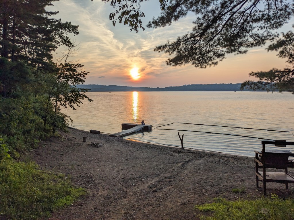 A sunset over Pleasant Hill Lake, the lake the camp is on.  A person is sitting at the end of a dock.