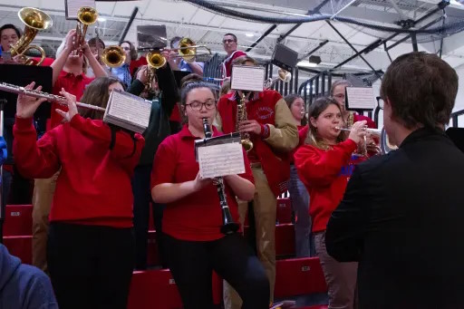 The pep band, in the stands of the gym, playing at a basketball game.